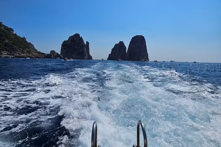Boat cruising towards the iconic Faraglioni rock formations in Capri's sparkling sea.