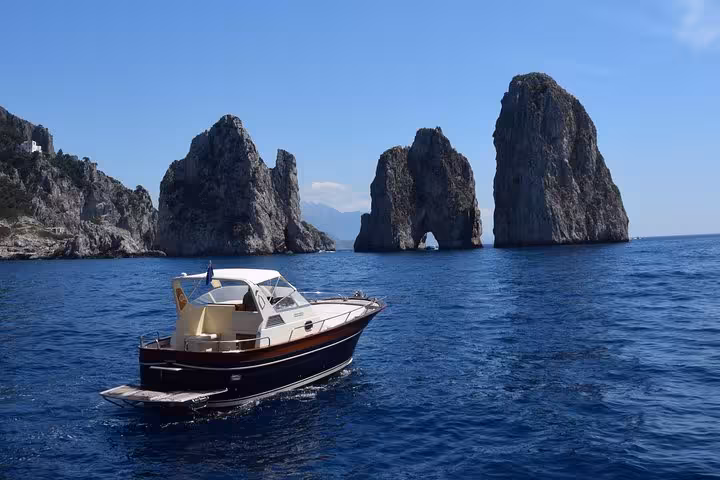 A scenic view of a boat navigating near the iconic Faraglioni rock formations on a Capri boat tour.