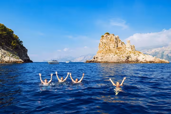 Group of friends swimming near iconic Capri cliffs on a small group boat tour from Positano.