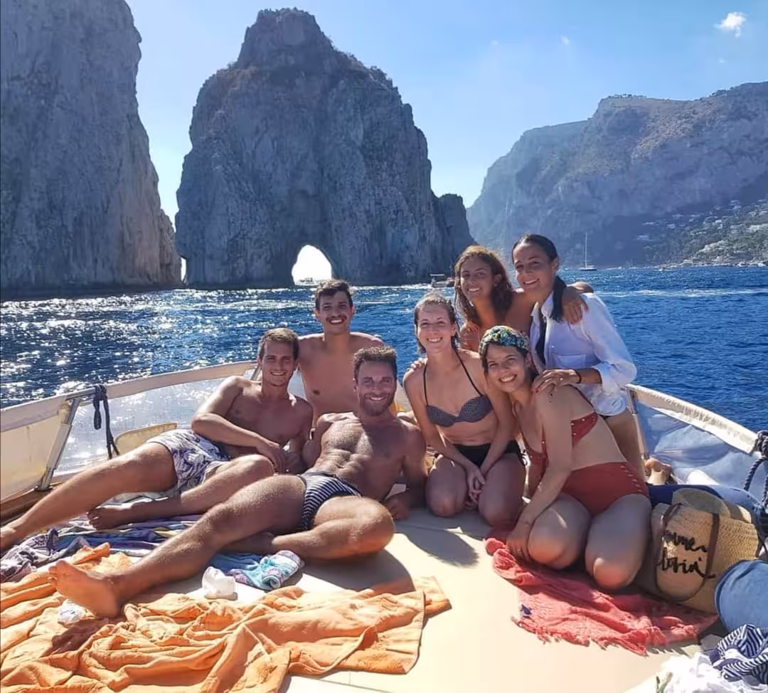 Group enjoying a sunny Capri boat tour with Faraglioni rocks in the background from Sorrento with Limoncello.