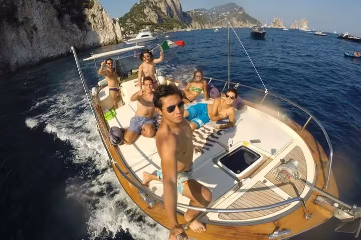 Group enjoying a scenic Capri boat tour from Sorrento, sunbathing on deck with limoncello, max 12 guests.