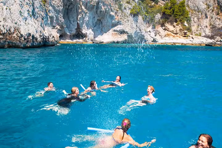 A group of people swimming and playing in the vibrant turquoise waters of Capri's coastline.