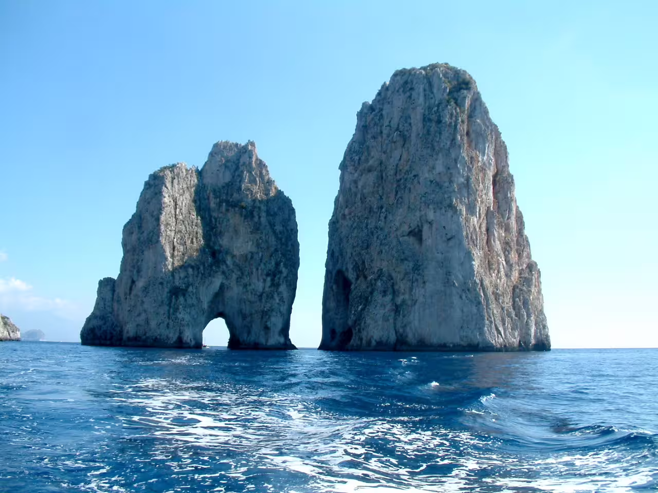 Faraglioni rock formations rising from the Tyrrhenian Sea on a clear-sky Capri boat tour along the coast