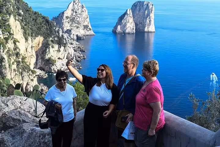 Group taking a selfie with stunning Faraglioni rock formations in Capri, a highlight of Naples coastal tours.