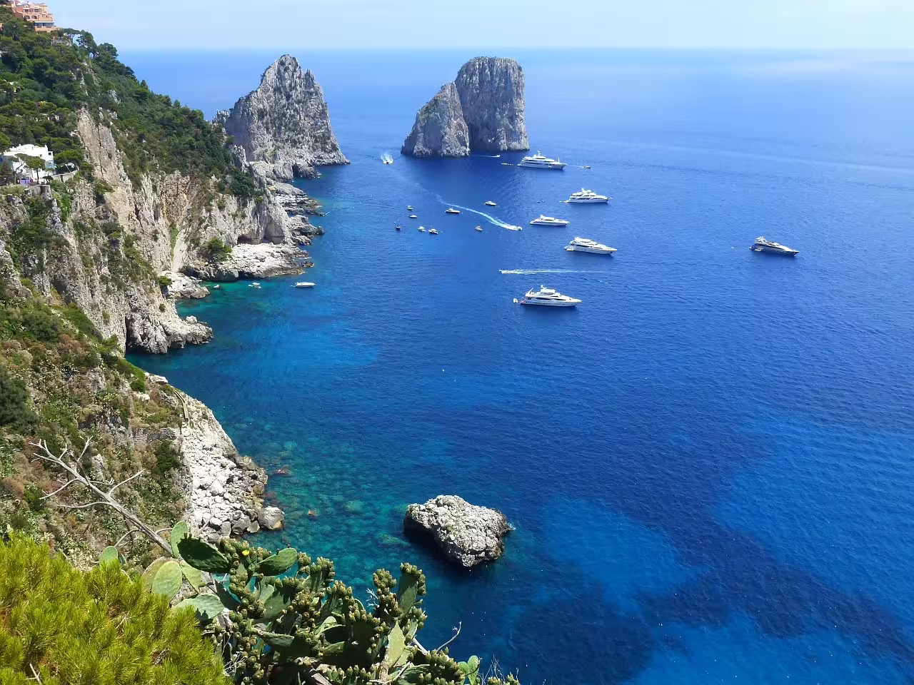 Luxury yachts cruising past Capri’s dramatic Faraglioni cliffs on a crystal-clear Tyrrhenian Sea boat tour experience