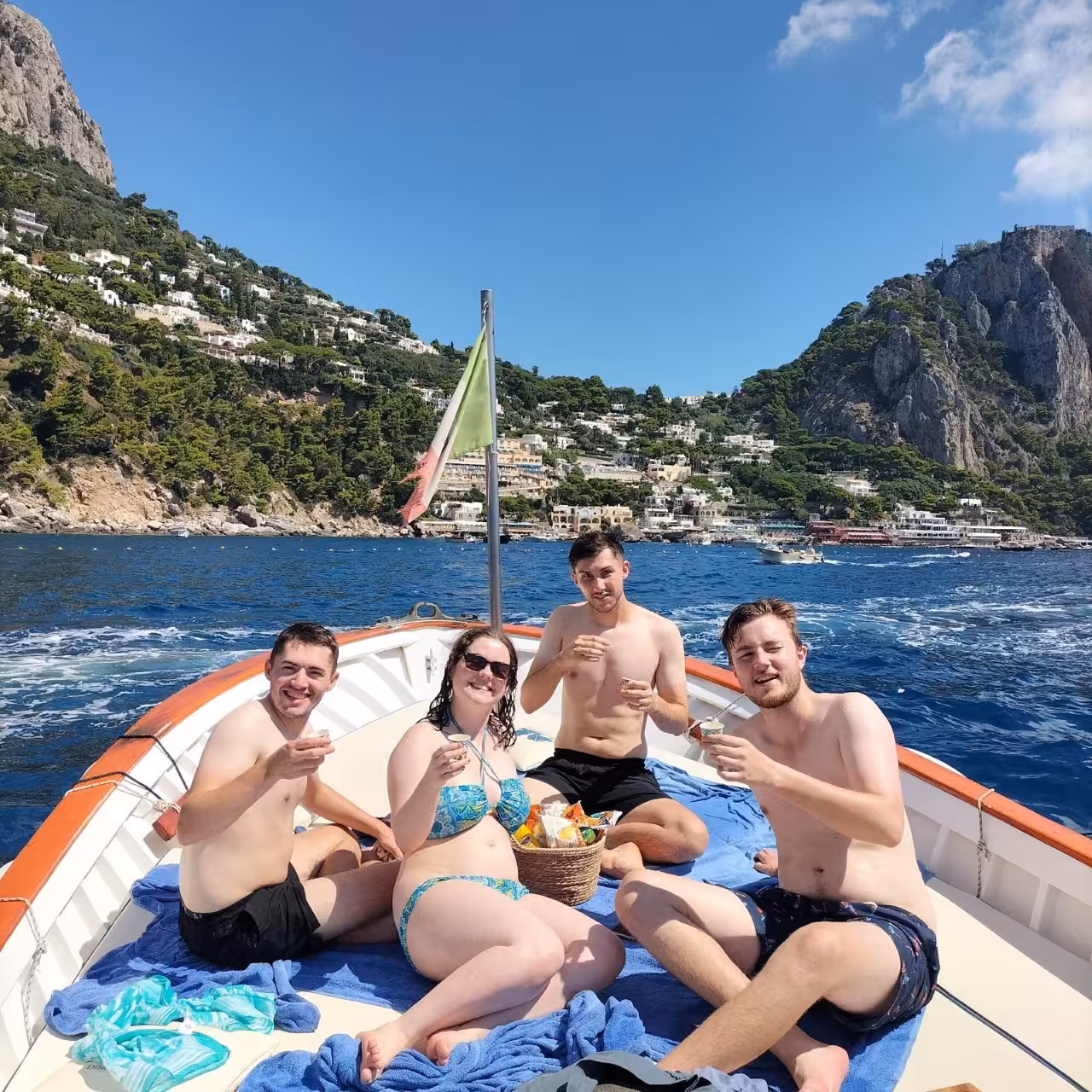 Friends relaxing on a private Capri boat tour with aperitifs, cruising past hillside villas and blue sea