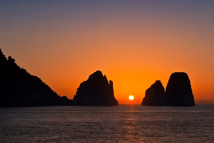 Stunning Capri sunset over Faraglioni rocks during a romantic boat tour experience.