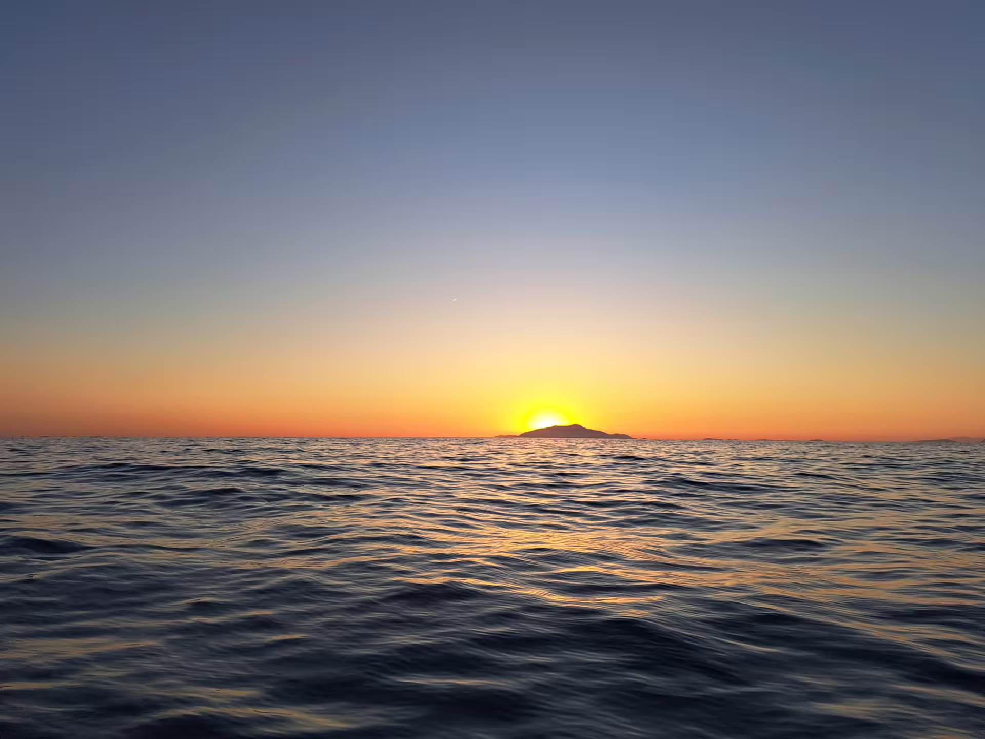 Sunset behind distant island over open water, From Dusk Till Night immersive night-world experience at sea