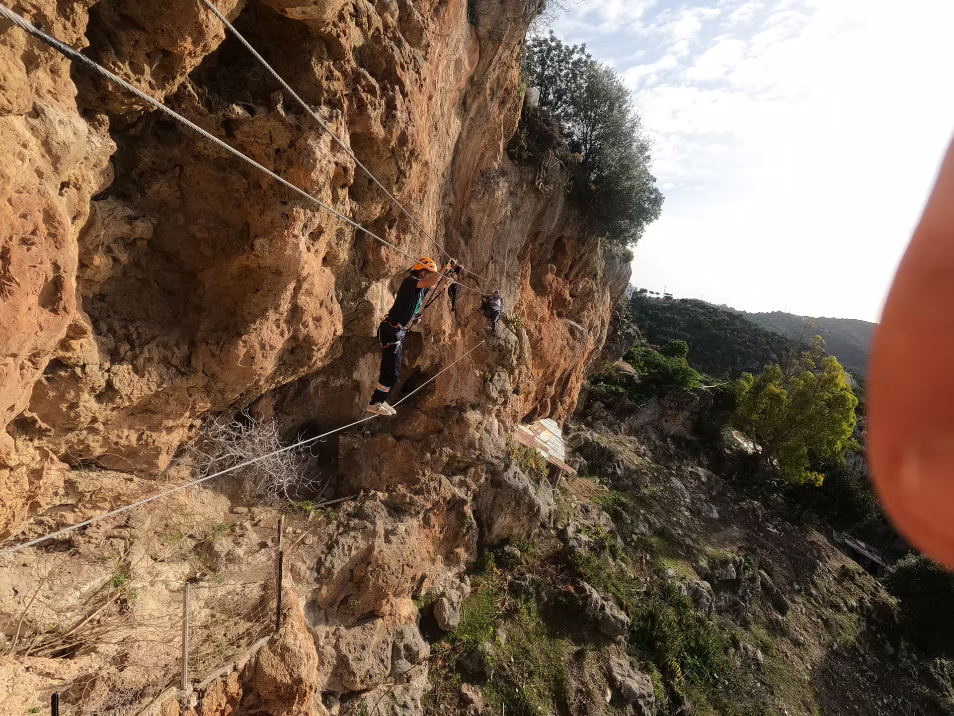 Adventurer on Casares Via Ferrata crossing rocky ledge with harness, offering thrilling climbing experience and stunning views.