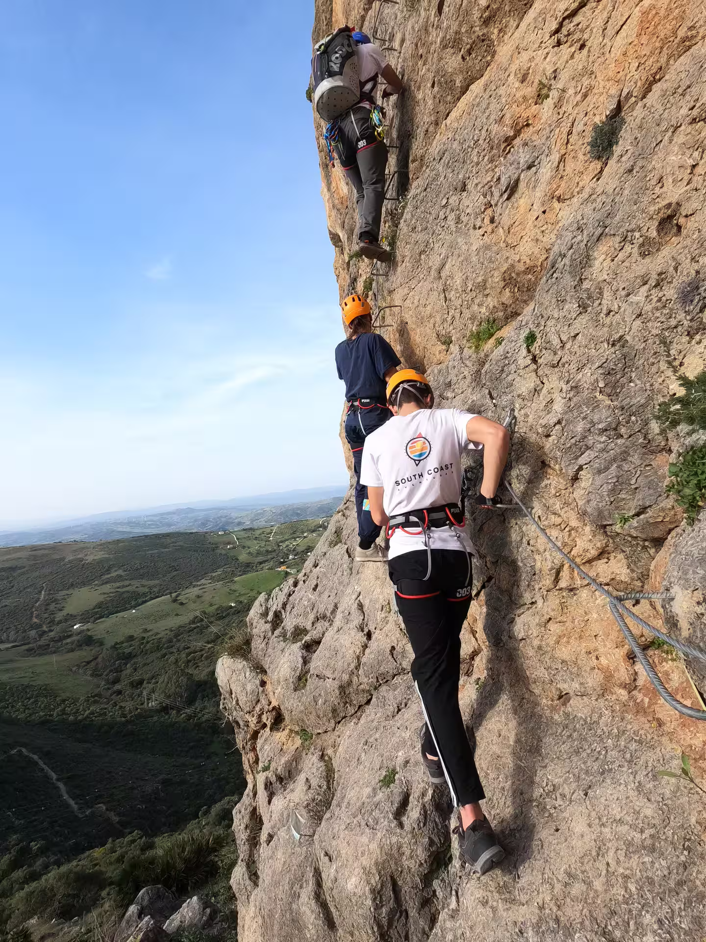 Group of adventurers climbing a vertical rock face on Casares' Via Ferrata, surrounded by stunning landscapes.