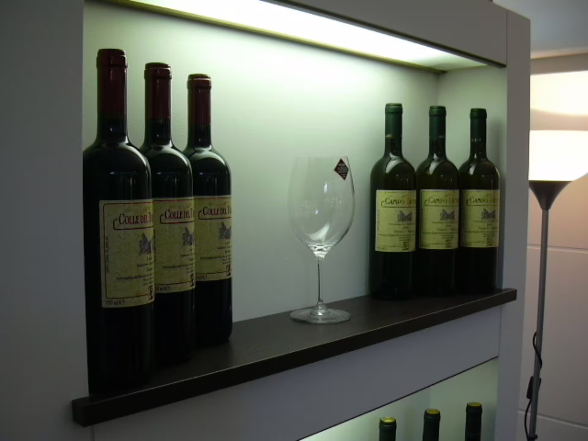 Wine bottles and a glass displayed on a shelf, highlighting the wine tasting experience at Castelli Romani.