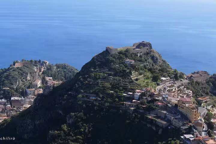 Scenic aerial view of Castelmola hilltop with ancient fortress and lush landscape overlooking the sea in Sicily.