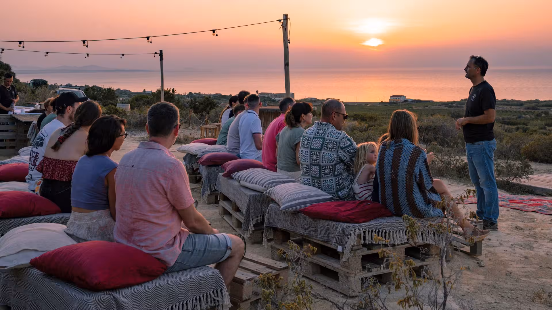 Guests seated on cushions enjoy a beautiful sunset view at a vineyard in Castelsardo during a wine tasting experience.