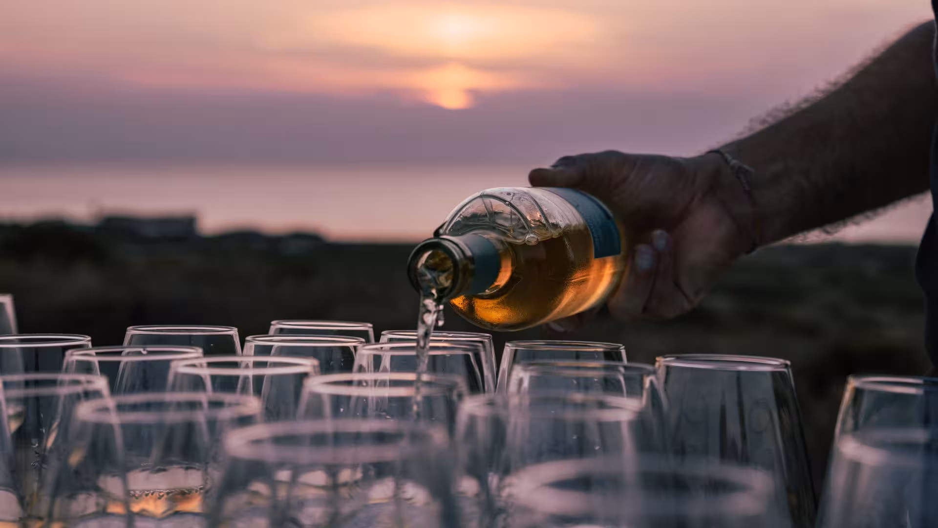 Wine being poured into glasses against a picturesque sunset backdrop in Castelsardo vineyard.