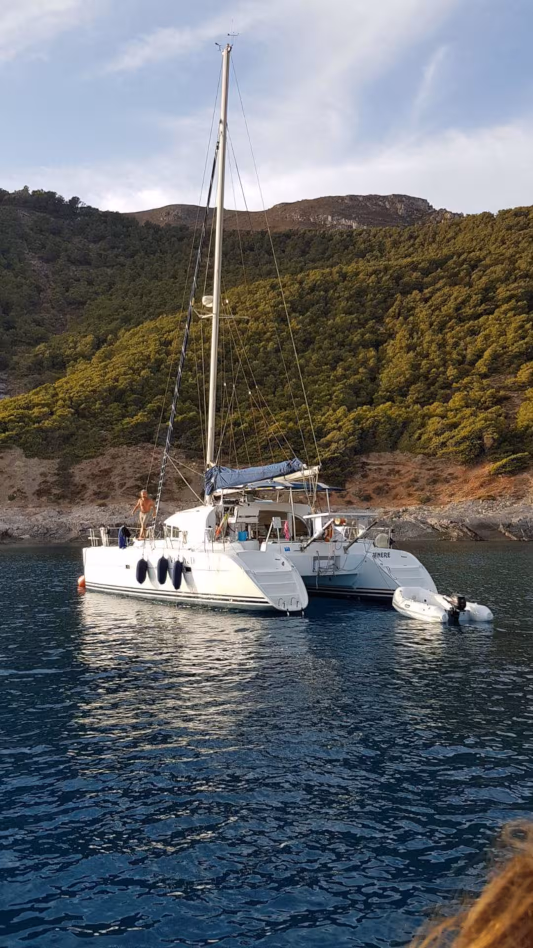 Catamaran Tenerè anchored in a serene bay of La Maddalena Archipelago, surrounded by lush green hills and calm waters.