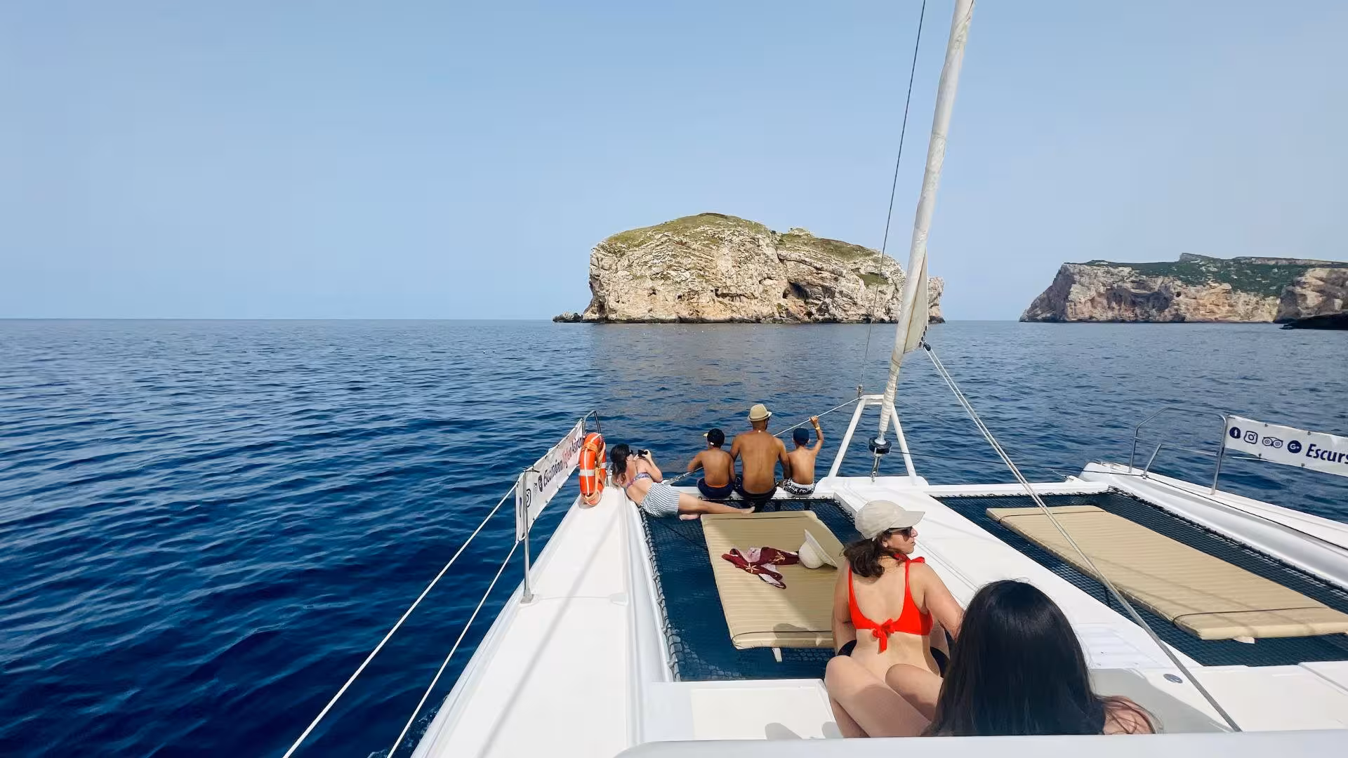 Tourists enjoying a scenic catamaran cruise in Porto Conte Park, Alghero, with stunning coastal views.