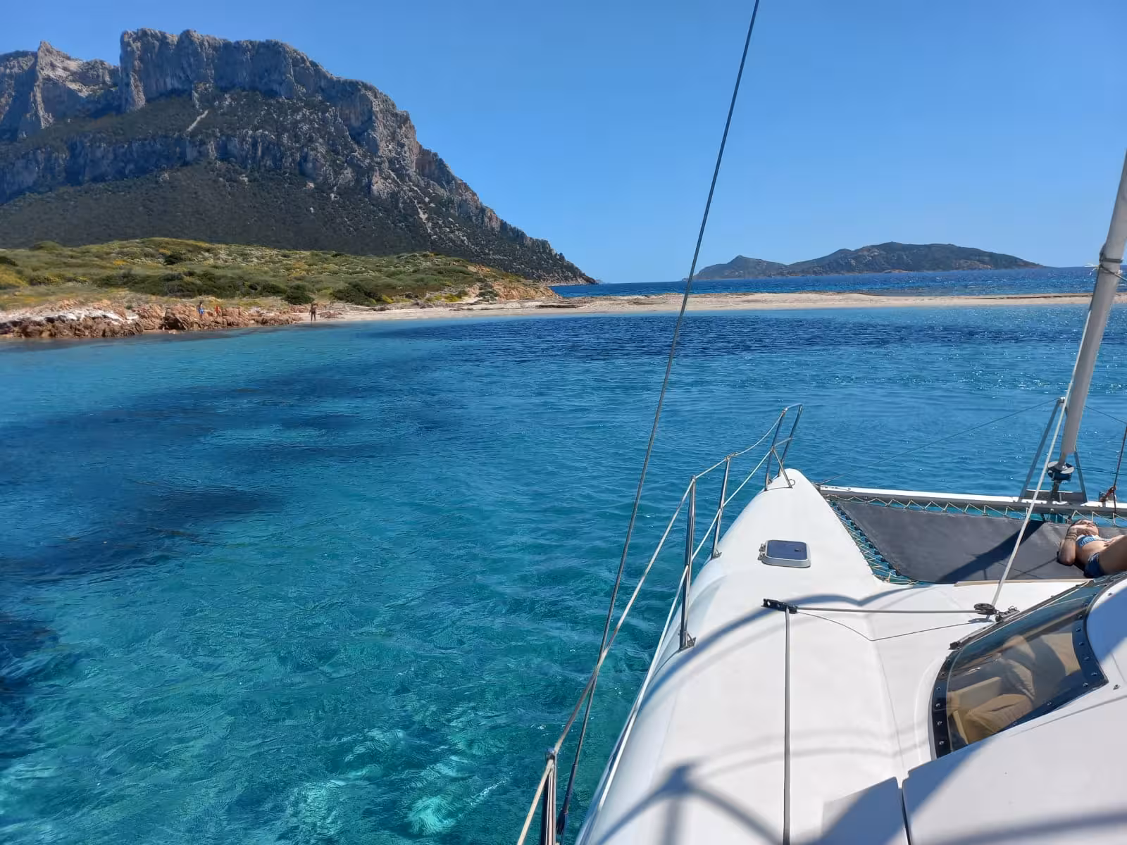 Catamaran sailing in clear turquoise waters near Tavolara Island, showcasing stunning coastal views and rugged cliffs.