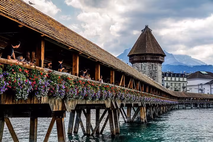 Historic Chapel Bridge in Lucerne adorned with vibrant flowers, offering scenic views of the Reuss River.