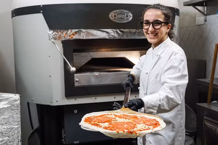 Smiling chef presenting freshly made pizza during a cooking class near Piazza Navona, Rome.