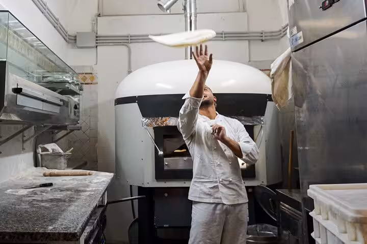 Chef tossing pizza dough in a traditional Roman kitchen, highlighting an engaging pizza-making class near Piazza Navona.