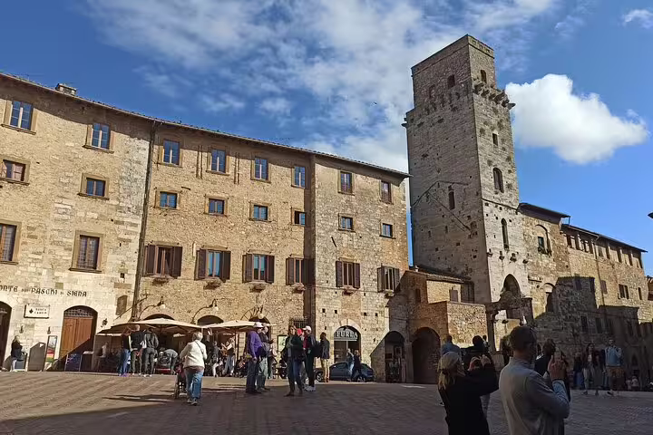 Tourists explore the medieval stone square and tower of San Gimignano on a sunny Chianti Classic wine tour in Tuscany, Italy