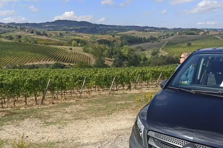 Private Chianti wine tour van parked beside panoramic Tuscan vineyards and hills on an afternoon visit to local wine farms