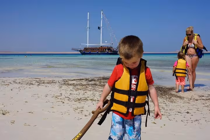 Child in life jacket on Orange Bay shore with Hurghada pirate sailing boat in background, family tour