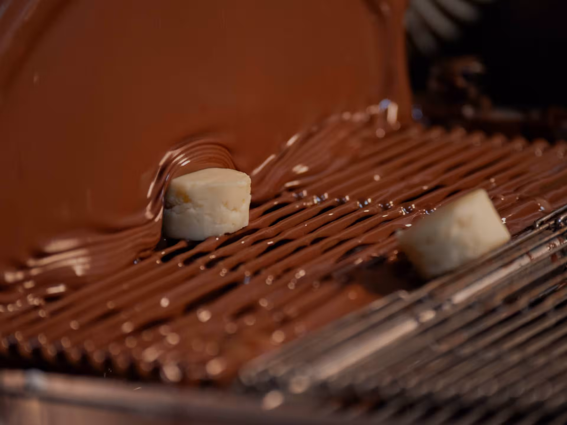 Close-up of biscuits being coated with rich chocolate on a conveyor at a Perugia chocolate factory tour.