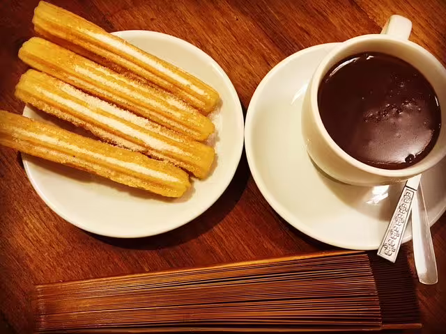 Plate of churros with a cup of thick hot chocolate on a wooden table, highlighting a classic Barcelona culinary experience.