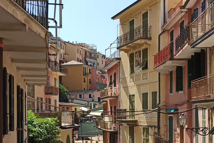 Narrow sunlit street lined with colorful pastel houses and balconies in a historic Cinque Terre village on a private day trip