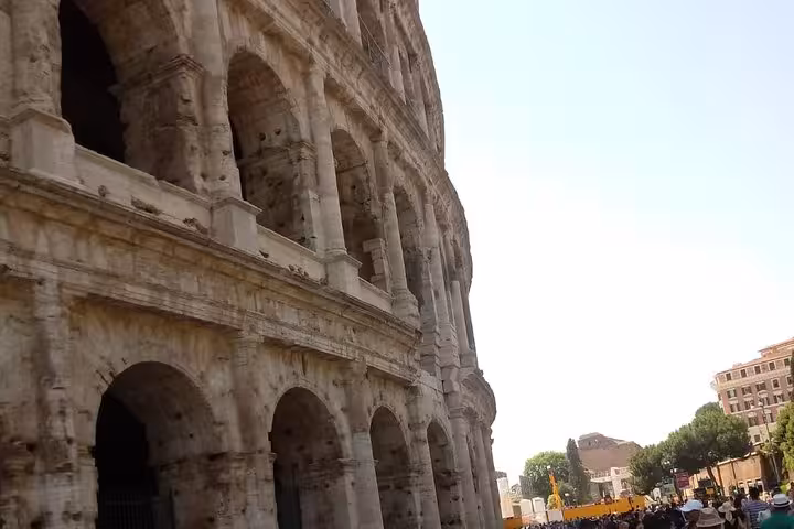 Side perspective of the Colosseum with clear blue sky, highlighting the grandeur of ancient Roman history.