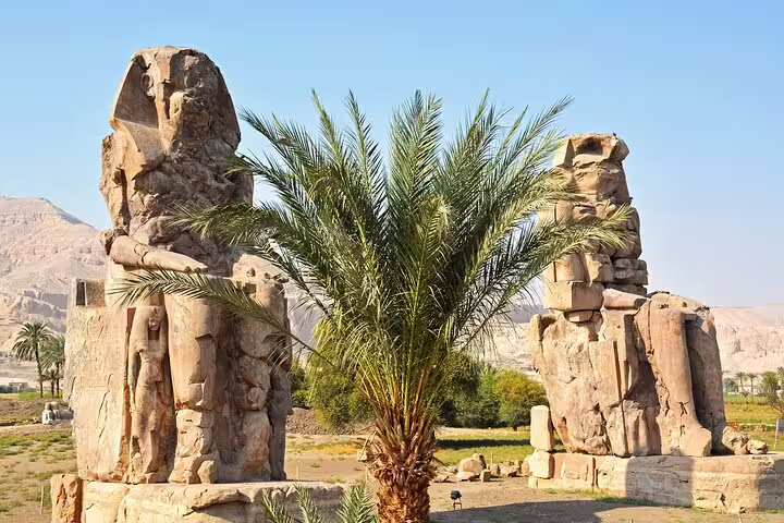 Colossi of Memnon statues near Luxor with palm tree, highlight of private Cairo to Luxor sleeper train trip