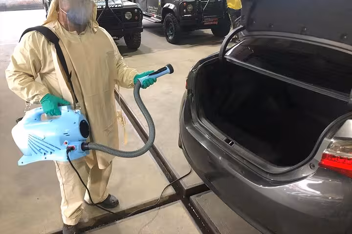 Professional sanitization of a car trunk by a worker in protective gear, ensuring safety for São Paulo transfers.