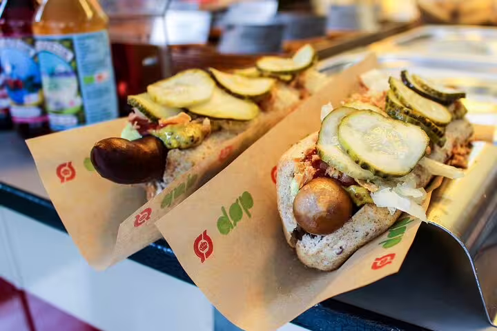 Gourmet Danish hot dogs topped with pickles and mustard on a Copenhagen food tour, showcasing local Scandinavian flavors.