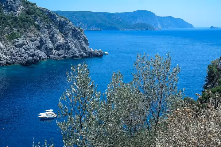 Boat on deep blue Corfu cove framed by cliffs and olive trees, Corfu Beauty & the Beach private tour view
