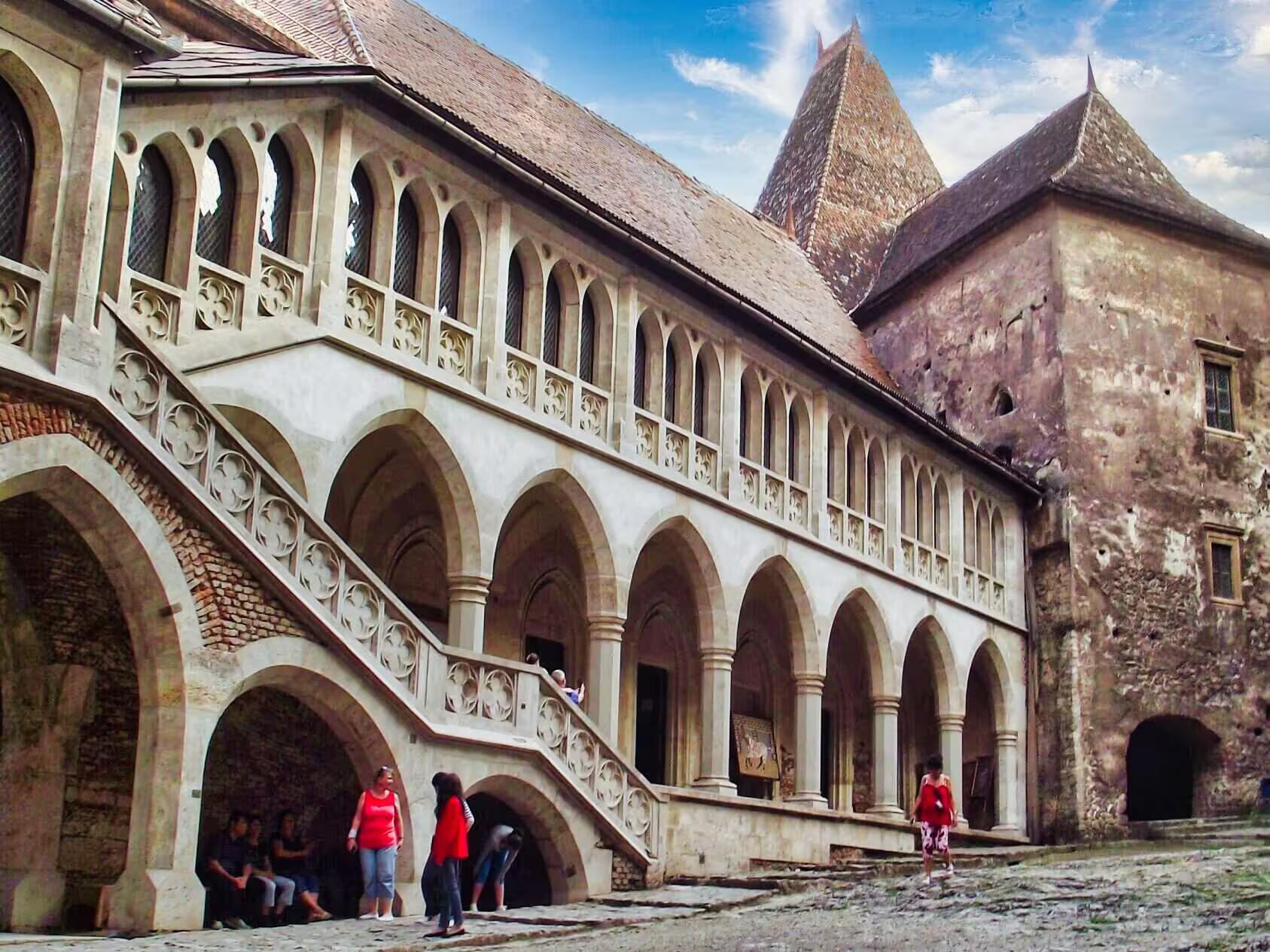 Gothic arcaded courtyard of Corvin Castle in Transylvania with tourists exploring medieval architecture on a guided tour