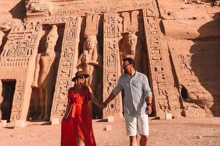 Couple at Abu Simbel Temple entrance on day tour from Aswan, admiring Ramses II carvings and hieroglyphs