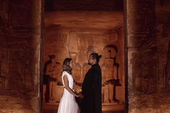 Couple standing inside Abu Simbel temple doorway with ancient carvings, romantic Aswan day trip in Egypt