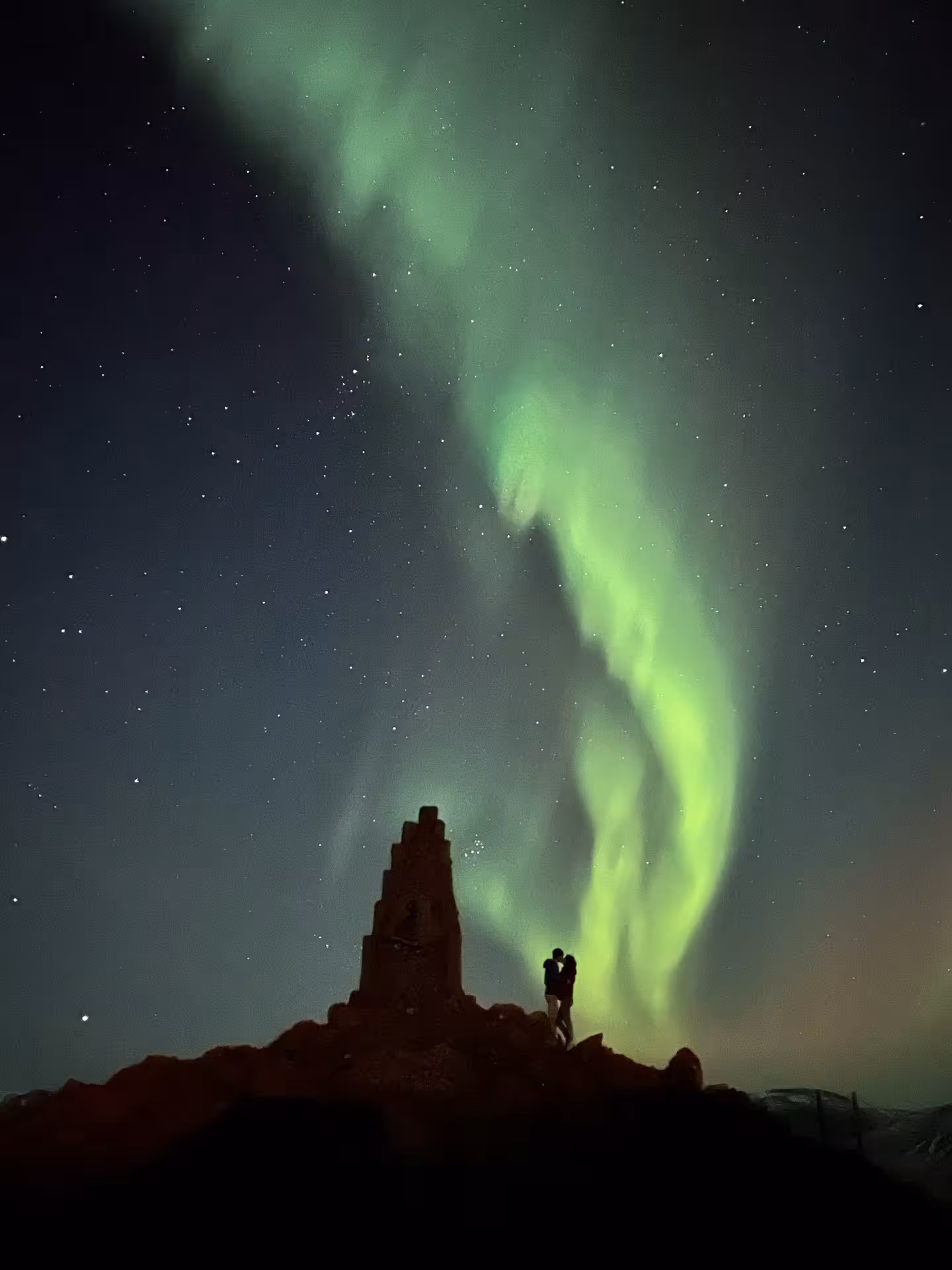 Couple silhouetted on Arctic ridge beneath vivid green Northern Lights on Adventure Arctic Odyssey aurora tour