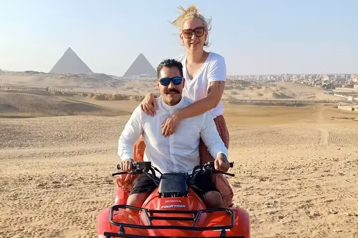 Couple posing on quad bike with Giza Pyramids backdrop, private ATV ride and camel tour with lunch in Cairo