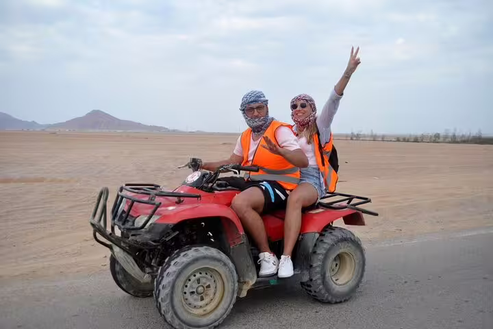 Couple riding double ATV quad bike in Sinai desert from Sharm El Sheikh, wearing safety vests and scarves