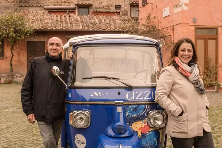 Smiling couple stands by a blue buggy in a charming Roman courtyard, showcasing the Valentine buggy tour.