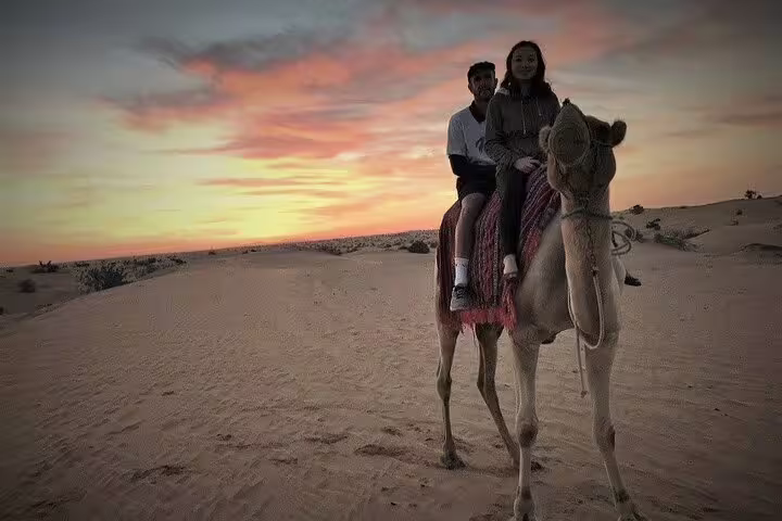 Couple enjoys a serene camel ride at sunset, showcasing the beauty of the desert landscape.