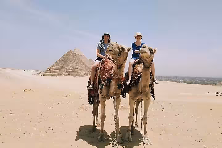 Couple on camels with the Giza Pyramid backdrop on a half-day private pyramids tour in Cairo with free ride