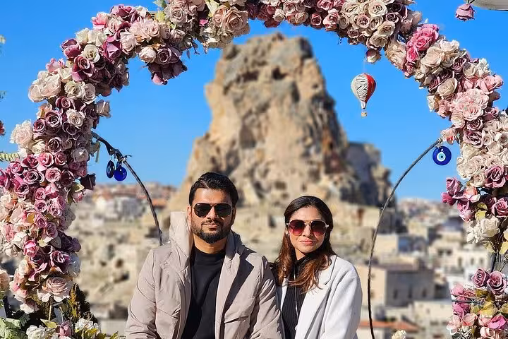 Couple at Cappadocia viewpoint under flower arch with fairy chimney and balloon on small group tour