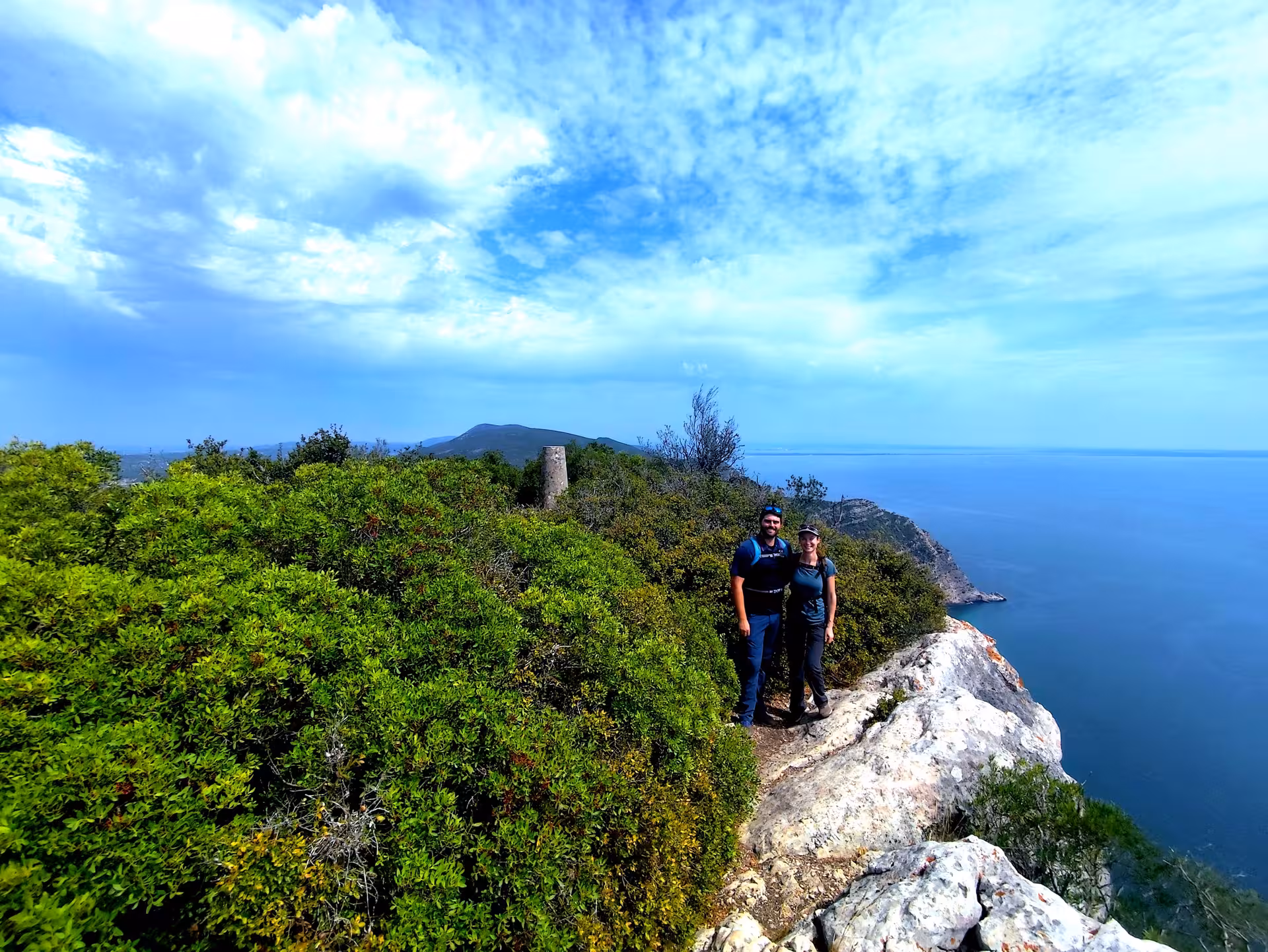 Couple on cliffside viewpoint during Arrábida Mountain highest point hike, overlooking Atlantic coast Portugal
