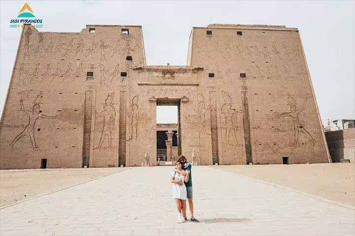 Couple posing at the massive Edfu Temple pylon, stop on a private Luxor day trip from Aswan by car