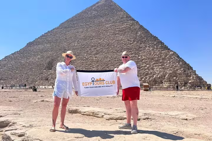Couple holding Egypt Tours Club banner in front of the Great Pyramid of Giza on Cairo private tour with Saqqara and Memphis