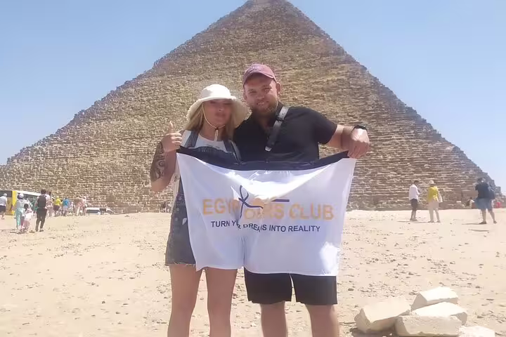 Couple holding tour banner in front of the Great Pyramid of Giza, private day tour with Grand Egyptian Museum stop