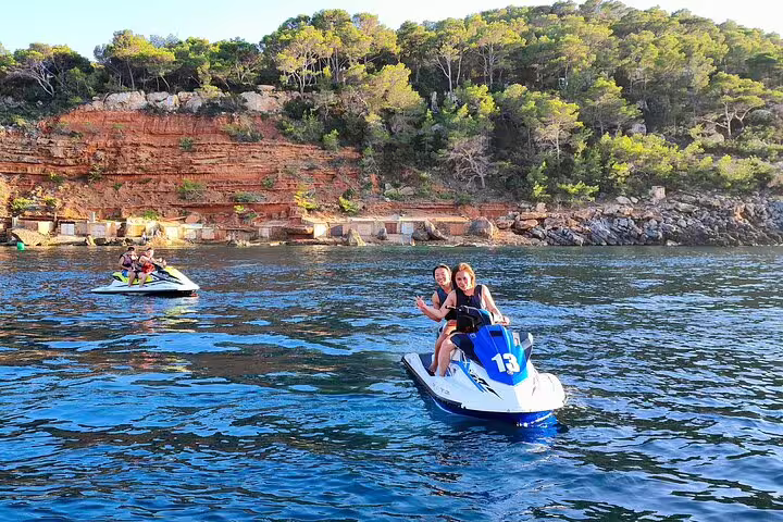 Couple riding a jet ski on guided tour to Cala Salada Ibiza, cruising past pine cliffs and clear sea